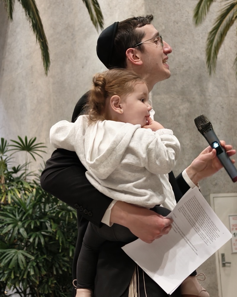 Rabbi Motti holding his daughter while speaking at a community event